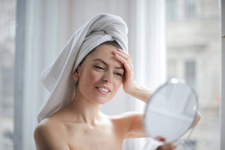 Woman wearing a towel on her head grimacing while looking in a mirror