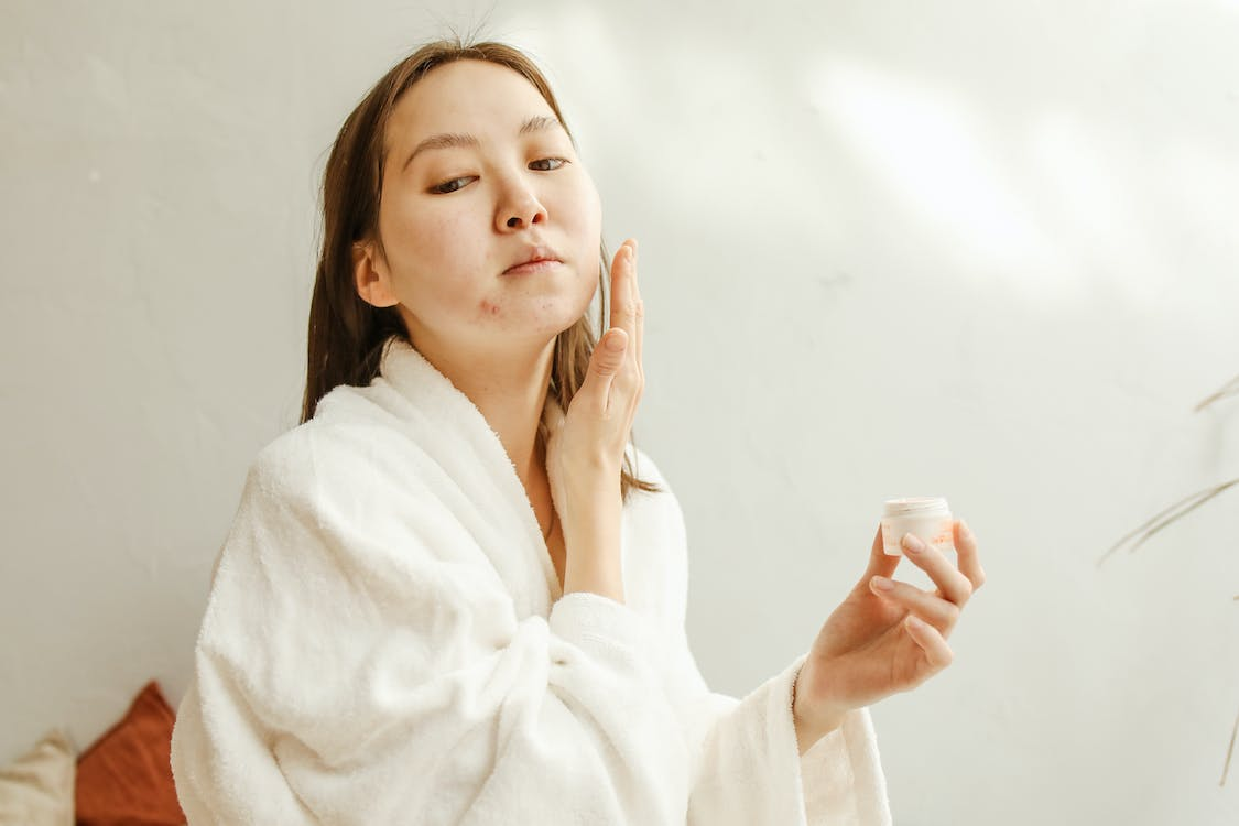 Woman with acne applying a facial cream