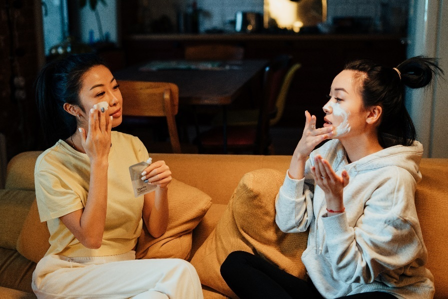 Two women sitting on a couch and applying cream on their face