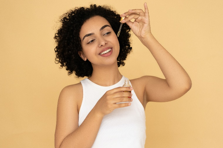 A person applying skincare on the face with a dropper.
