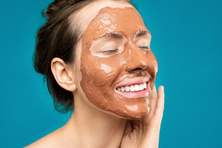 A woman smiling with a clay face mask on